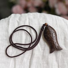 a long brown cord with a fish shaped pendant hanging from it's end on top of a white pillow