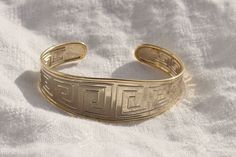 a close up of a gold bracelet on a white cloth with the word mean written in cursive writing