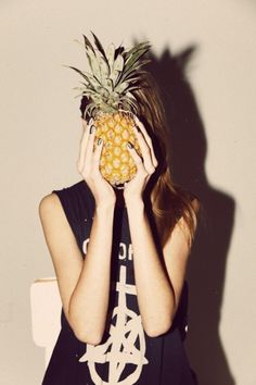 a woman holding a pineapple up to her face