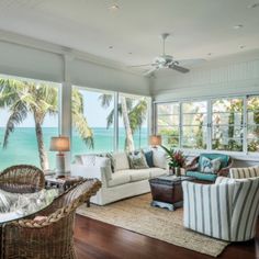 a living room filled with lots of furniture and large windows overlooking the ocean on top of a wooden floor