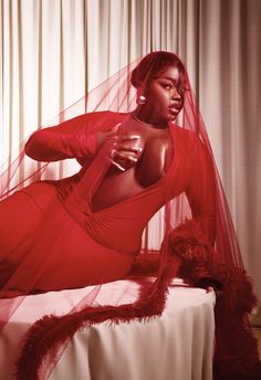 a woman in a red dress sitting on a bed with a veil over her head