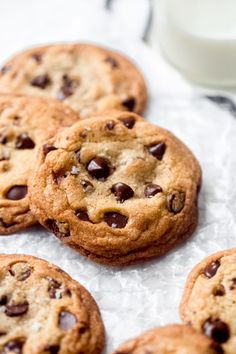 several chocolate chip cookies sitting on top of a piece of paper next to a glass of milk