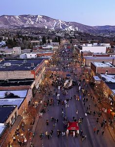 an aerial view of a city street with people walking on the sidewalks and snow covered mountains in the background