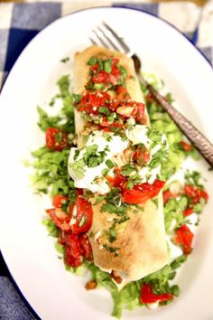 two burritos with tomatoes, lettuce and feta cheese on a white plate