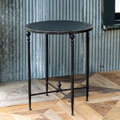 a black table sitting on top of a wooden floor next to a metal wall covered in peeling paint