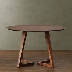 a round wooden table with two triangular legs on a hard wood floor in front of a green wall