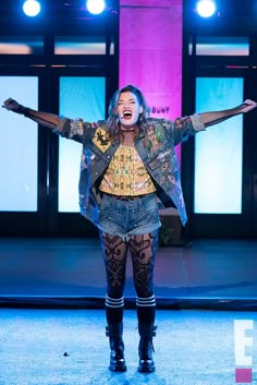 a woman in tights and boots standing on stage with her arms spread wide open