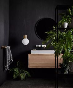 a bathroom with black walls and plants in the corner, along with a round mirror on the wall