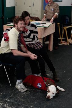 three people sitting at a table with a dog on the floor next to them,