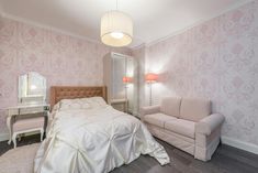 a white bed sitting next to a couch in a room with pink wall paper on the walls