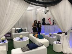 two women standing next to each other in a room with white couches and tables