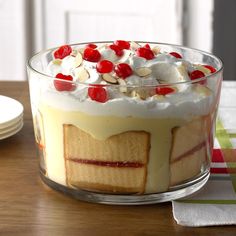 there is a dessert with cherries on top in a glass bowl next to plates