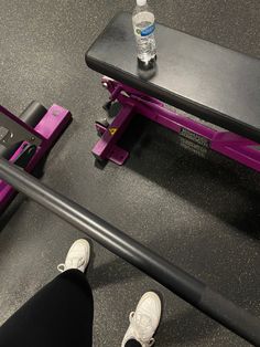 a person standing next to a purple bench with water bottle on it and black barbells in the background