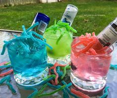 three different colored cocktails sitting on top of a table next to bottles and scissors