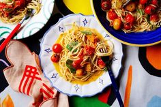 two plates of pasta with tomatoes and other food items on a colorful cloth tablecloth