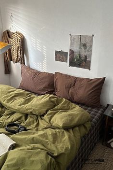 an unmade bed in a bedroom with green sheets and brown pillows on top of it