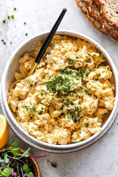 a bowl filled with scrambled eggs and topped with parsley next to slices of bread