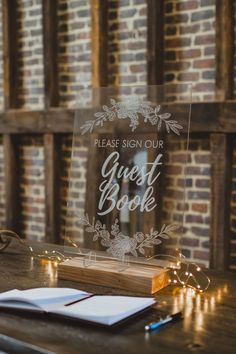 a clear acrylic sign that says guest book on top of a wooden table