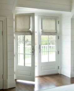 the inside of a house with two white doors and windows that have shades on them