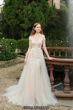 a woman standing in front of a fountain wearing a wedding dress with sheer neckline