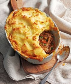 a pot pie with meat in it on top of a wooden cutting board next to a spoon