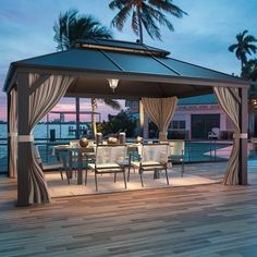 a gazebo with chairs and tables on a deck next to the ocean at dusk