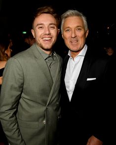 two men standing next to each other wearing suits