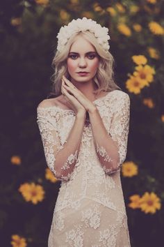 a woman wearing a white dress standing in front of flowers with her hands on her chest