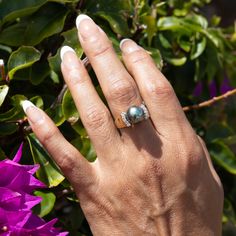 a woman's hand with a ring on it and purple flowers in the background