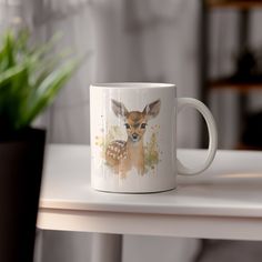 a coffee mug with a deer on it sitting on a table next to a potted plant