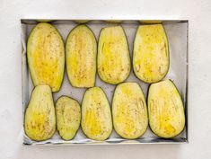 several pieces of yellow squash in a metal pan on a white surface with black speckles