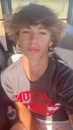 a young man sitting in the back seat of a car with his hair blowing in the wind