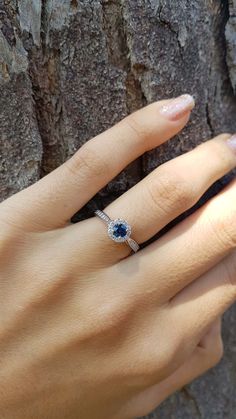 a woman's hand with a ring on her finger next to a tree trunk