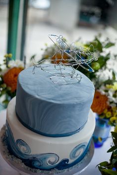 a blue and white cake sitting on top of a table next to some flower arrangements