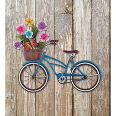 a blue bicycle with flowers in the basket on a wooden fence wall hanging from it's side