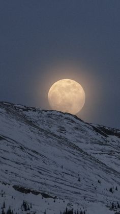 the full moon is seen over a snowy hill