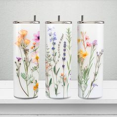 three white vases with colorful flowers painted on them sitting on a shelf next to each other