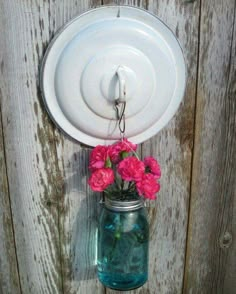 a mason jar with pink flowers hanging from it's side on a wooden fence