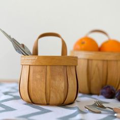 two wooden baskets sitting on top of a table next to oranges and silverware