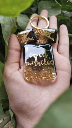 a hand holding a black and gold square shaped keychain