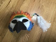 a stuffed animal with feathers on it's head sitting on the floor next to a feather keychain