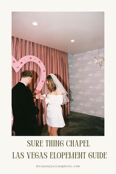 a man and woman standing next to each other in front of a heart shaped sign