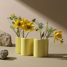 three yellow vases with flowers in them sitting on a table next to rocks and a rock