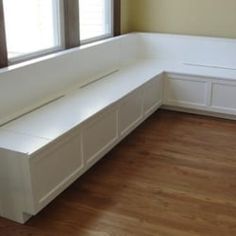 a white bench sitting in the middle of a room next to a window and wooden floor