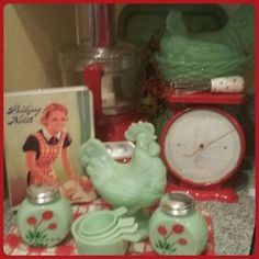 an assortment of green vases and clocks on a red tablecloth with a book