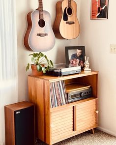 two guitars are hanging on the wall above a record player's cabinet and stereo