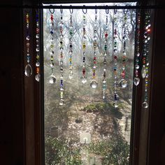 a window with beads hanging from it's side and trees in the back ground