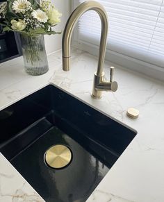 a kitchen sink with a gold faucet and marble counter top next to a window