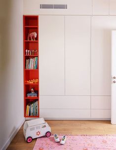 an orange book shelf in the corner of a room with books and toys on it