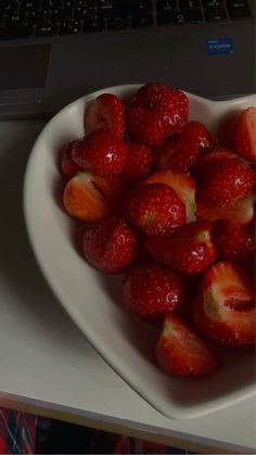 a heart shaped bowl filled with strawberries next to a laptop